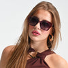 Woman wearing sunglasses and a brown top against a light background