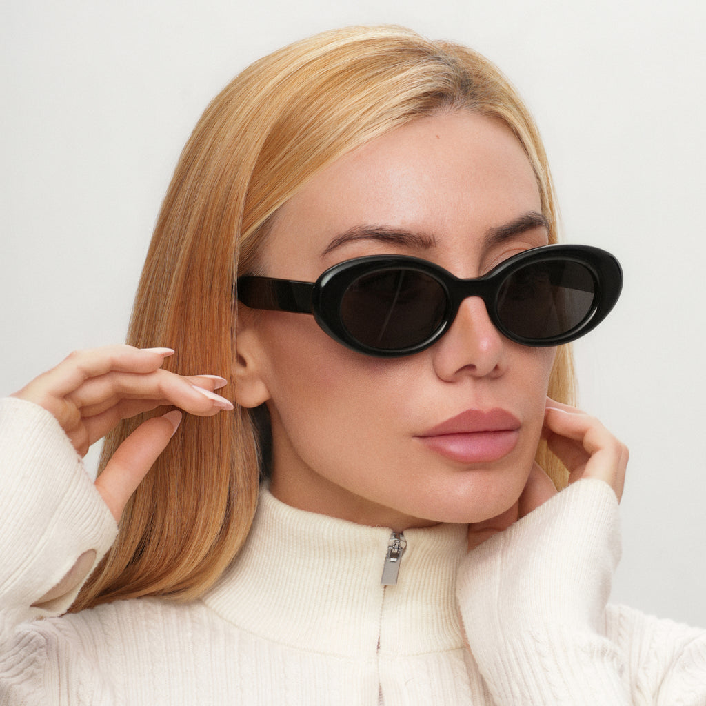 Woman wearing black cat-eye sunglasses against a light background