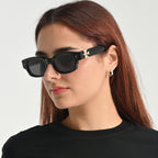 Woman wearing black sunglasses with a gold accent on a plain background