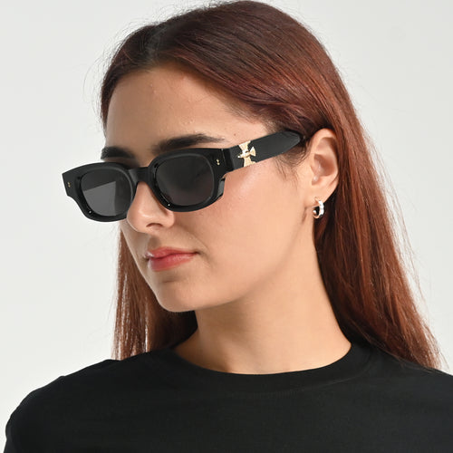 Woman wearing black sunglasses with a gold accent on a plain background