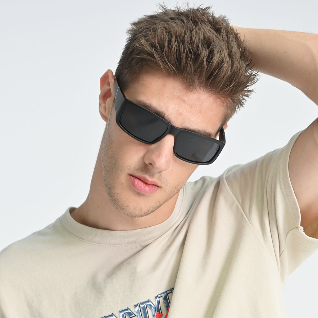 Man wearing black sunglasses and a beige t-shirt against a light gray background