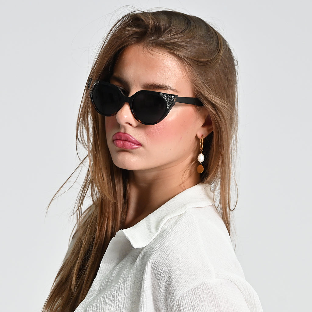 Woman wearing black cat-eye sunglasses against a light gray background