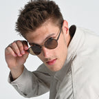 Man wearing sunglasses and a light-colored jacket against a plain background