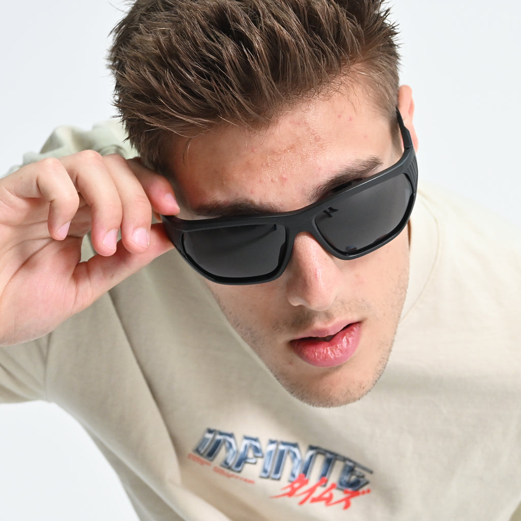 Man wearing black sunglasses with a light-colored shirt featuring text