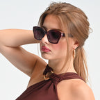 Woman wearing sunglasses and a brown top against a light background
