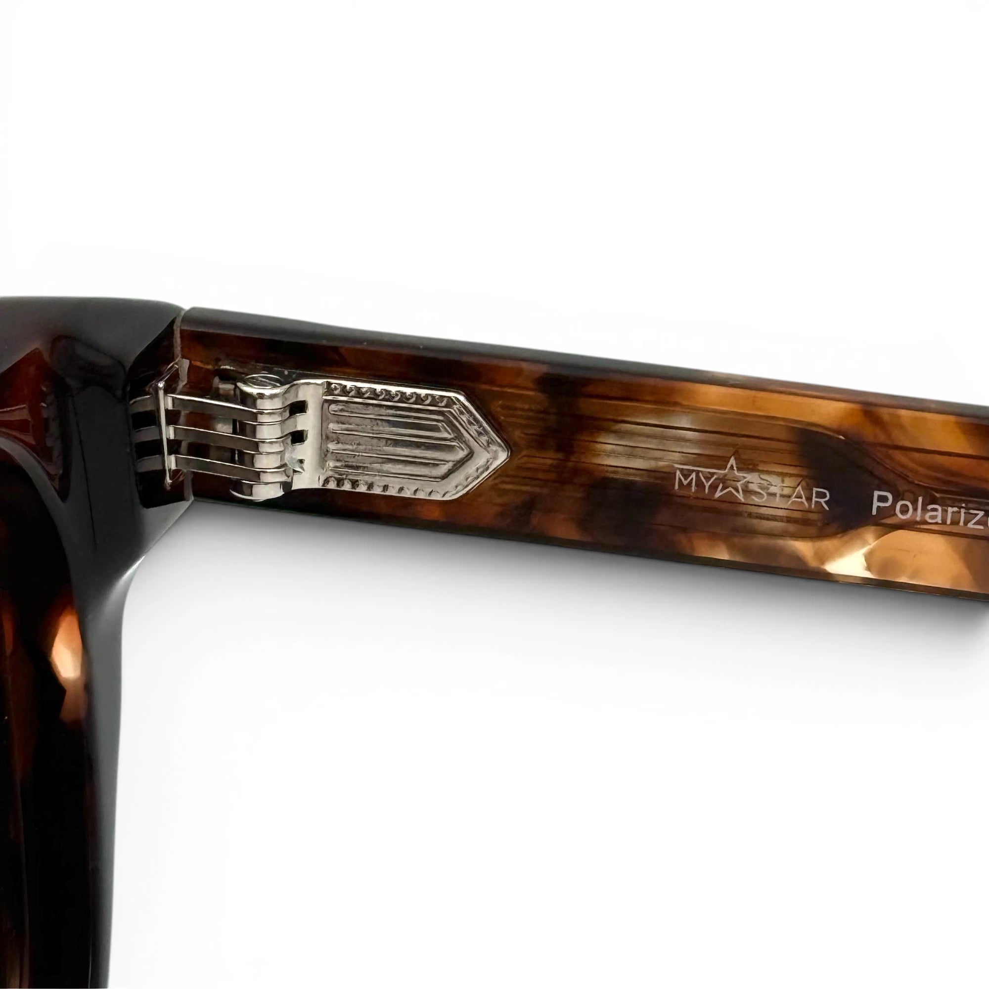 Close-up of a tortoiseshell sunglasses frame with metallic hinge on a white background