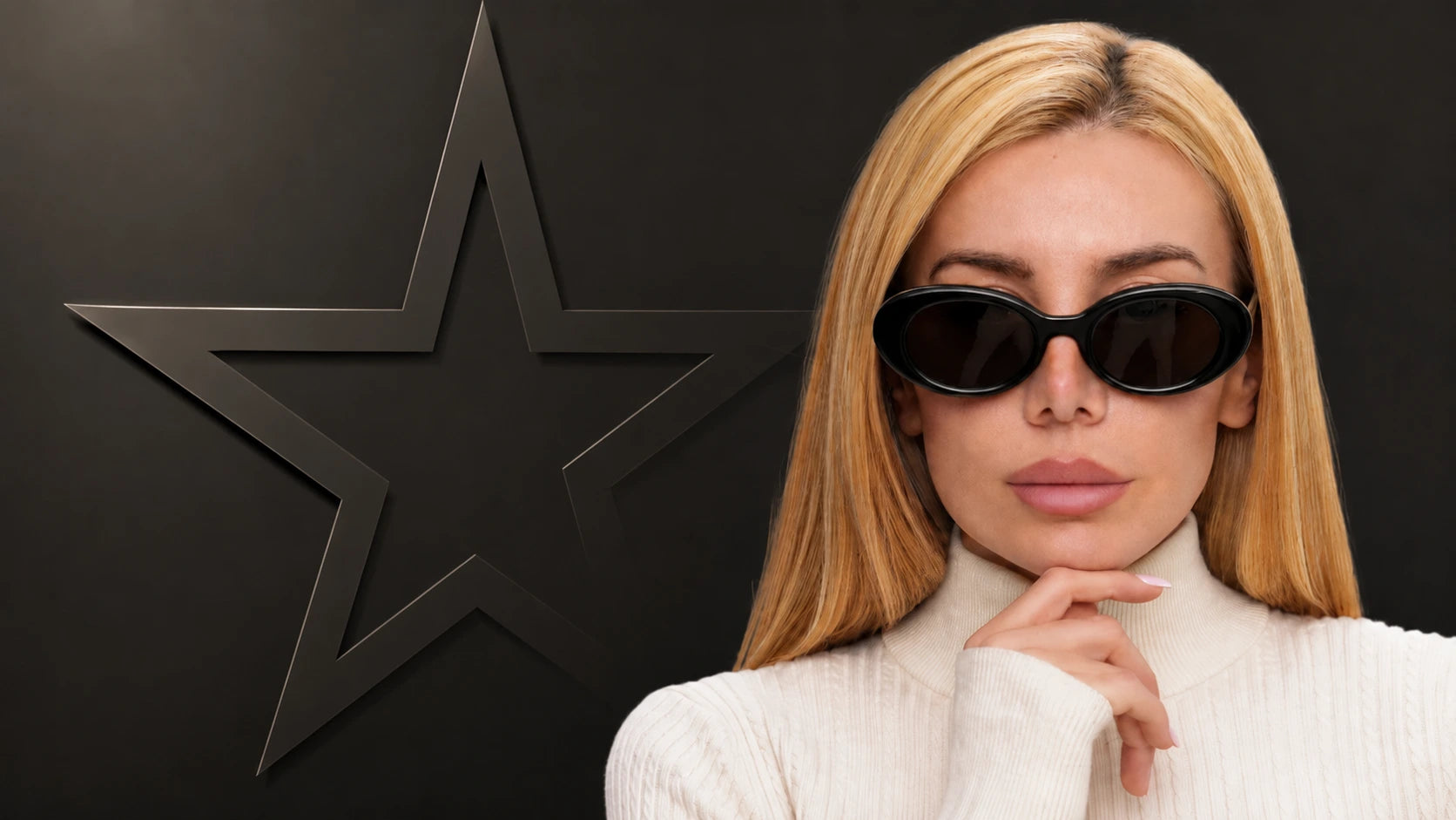 A blonde woman wearing black cat-eye sunglasses and a white ribbed turtleneck sweater, posing against a dark gray background with a large black star-shaped wall art piece.